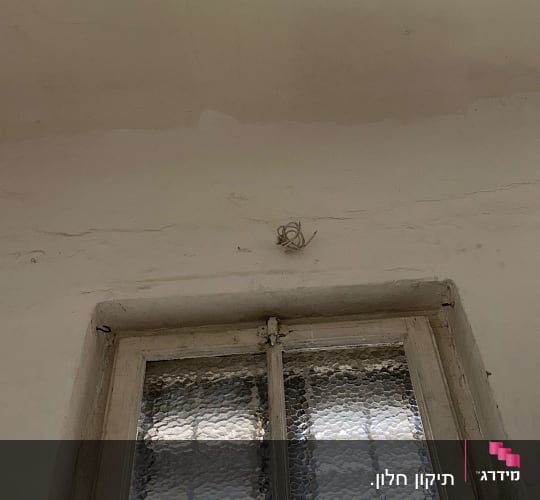 חלון זכוכית עם מסגרת ישנה על קיר לבן